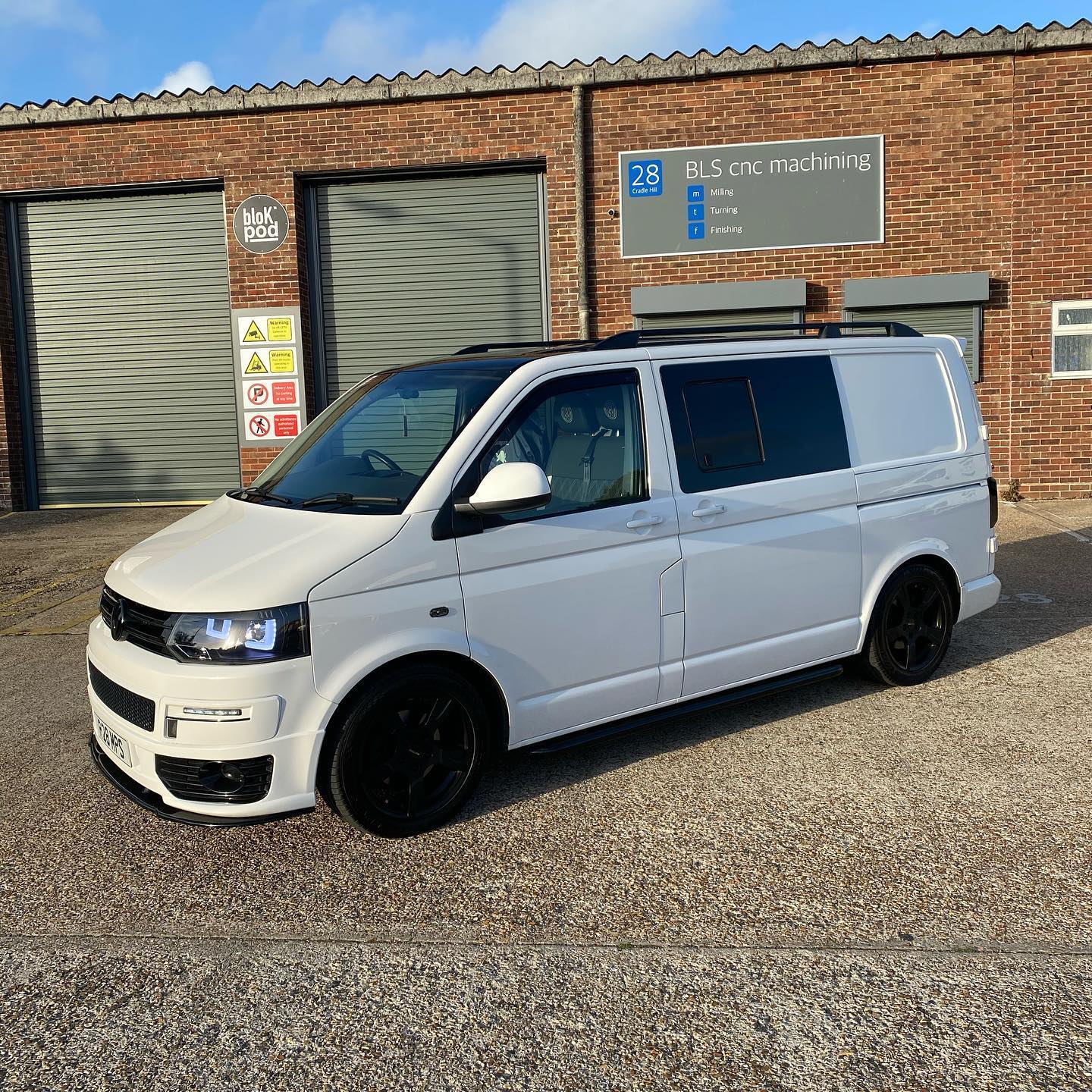 A white van parked in front of a building, showcasing its side view so you can see all windows.