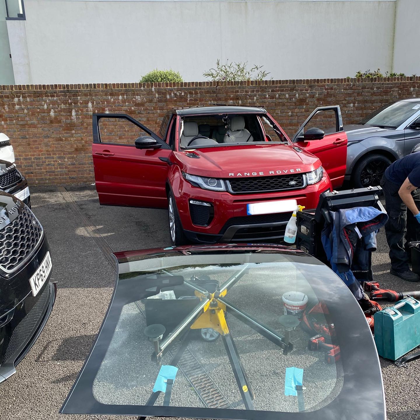A man fitting a new windscreen into a red Range Rover, focused on his work with tools nearby.